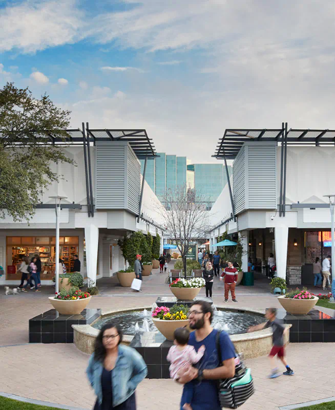 Groups of people walk and talk as they make way across the green lawns of Biltmore Fashion Park.