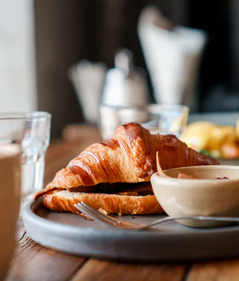 A croissant sandwich sits on a gray plate and is served with fresh fruit.