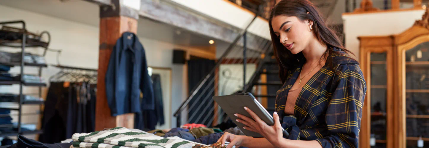 A woman touches the fabric of a green lined shirt while looking at an iPad.