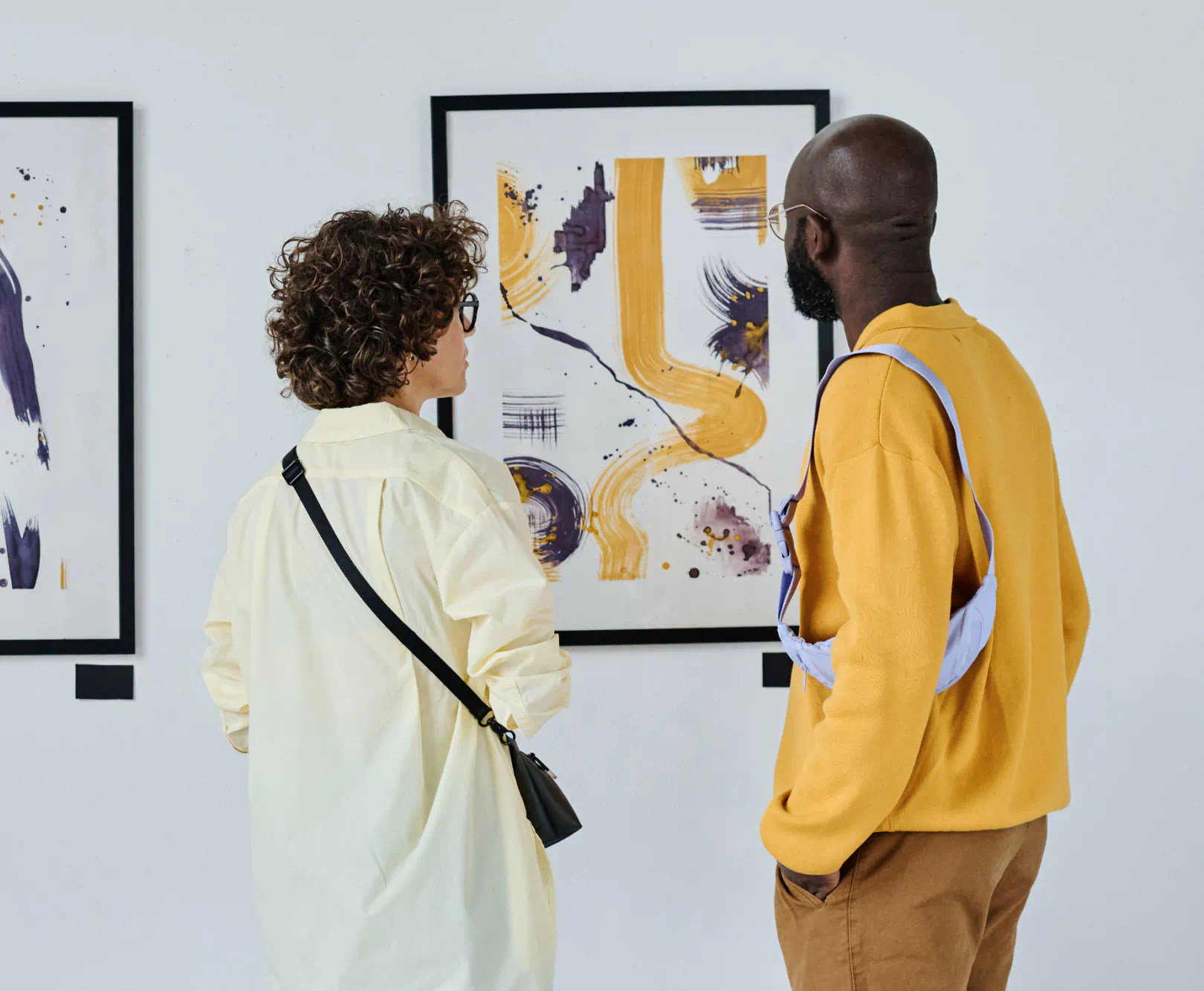 Two people admire some modern art on a white wall. Both are dressed in yellow shirts.