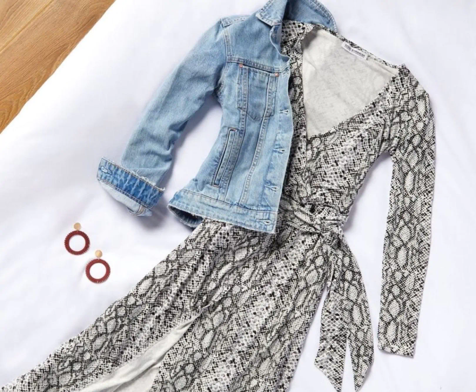 A dress with a snakeskin pattern and denim coat sit on a white cloth.