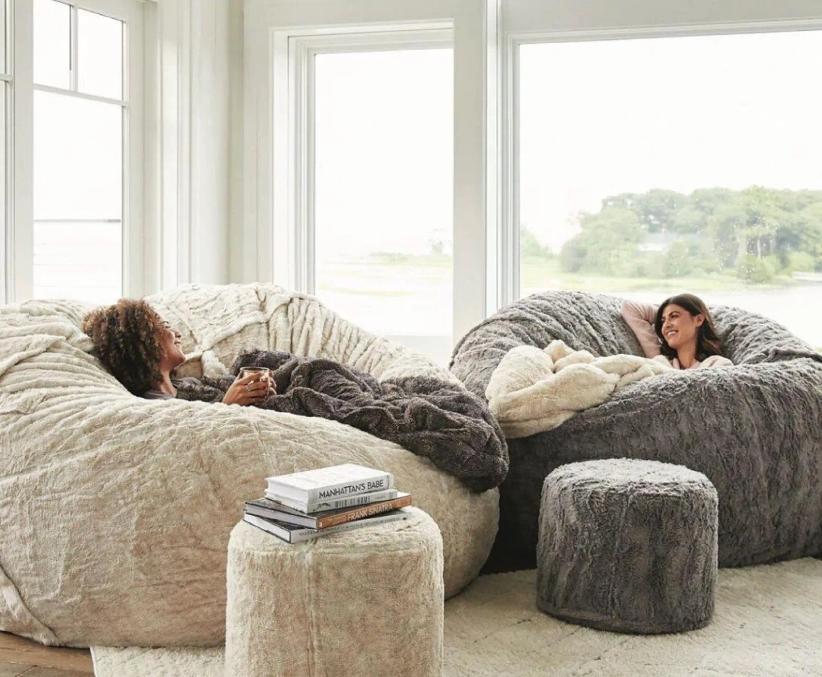 Two woman talk and drink tea as they sit in large, tan beanbag chairs.