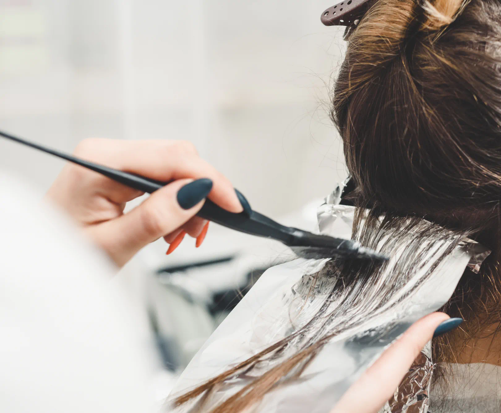 A hairdresser applies layers of color to a woman's hair using a brush.