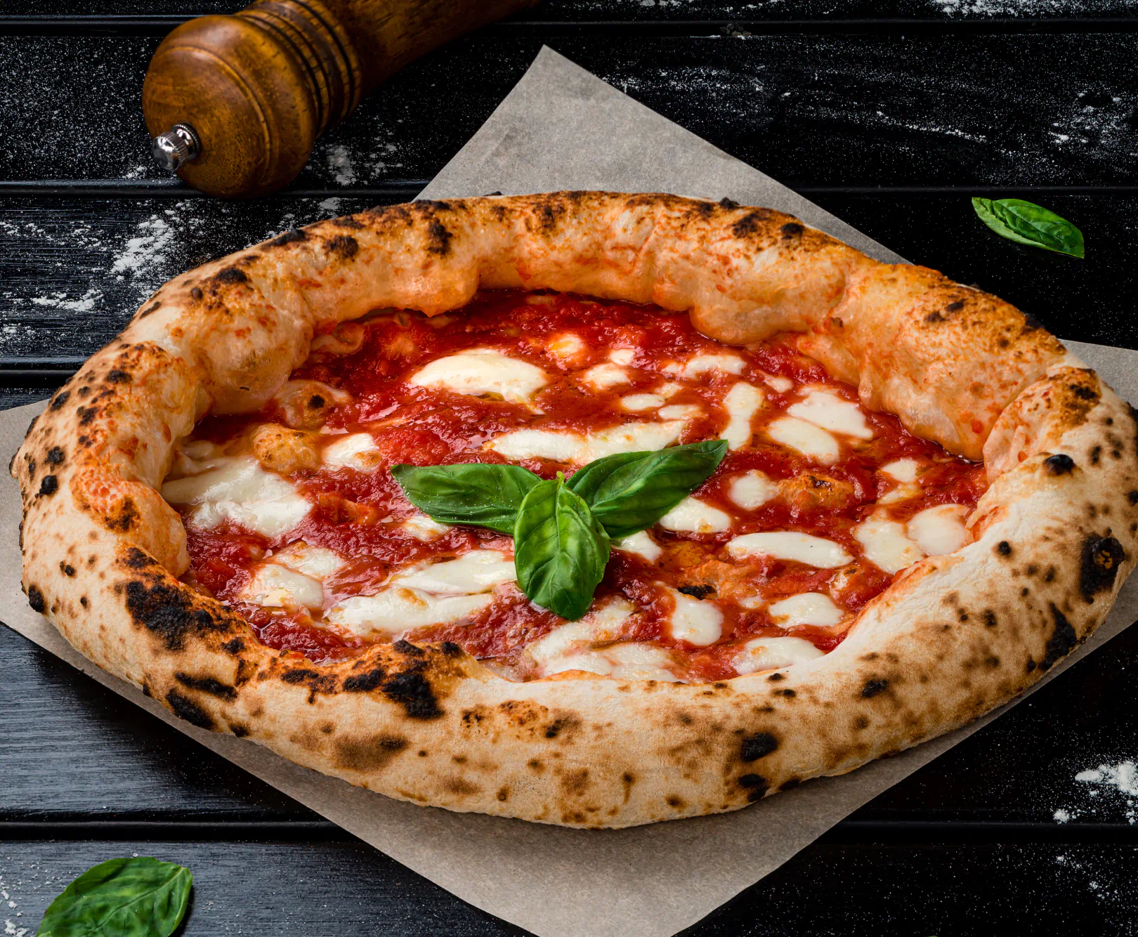 A margarita pizza sits atop a piece of parchment paper surrounded by grains of salt.