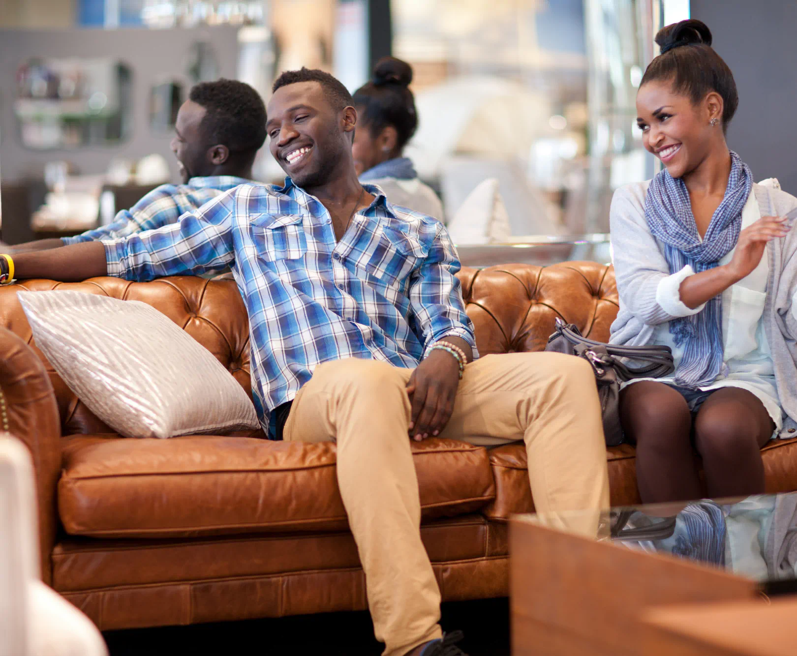 A couple sits on a large lather couch and smile as the enjoy the texture of the surface.