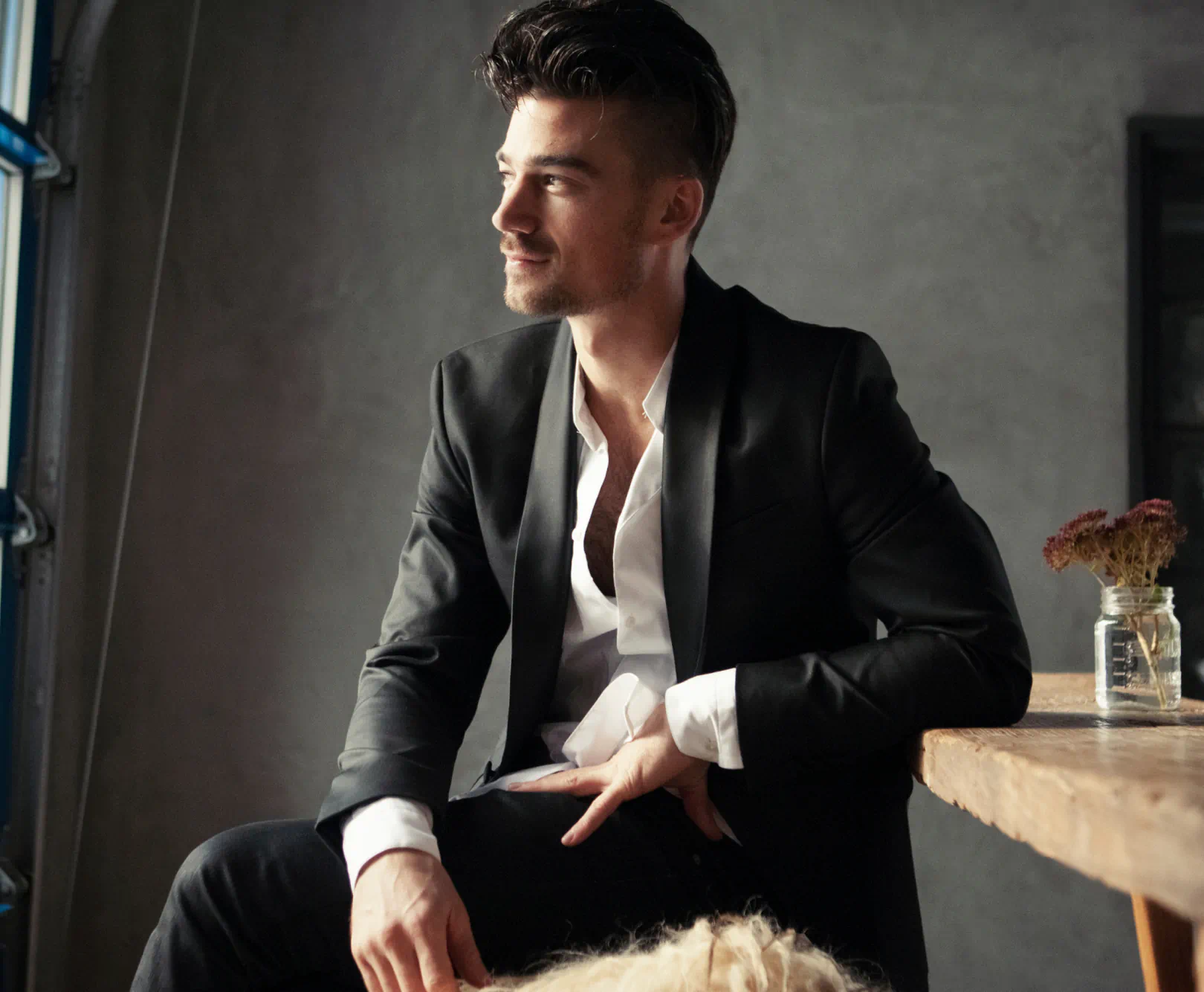 A man in a well-tailored suit and buttoned downed shirt stares out of a window.