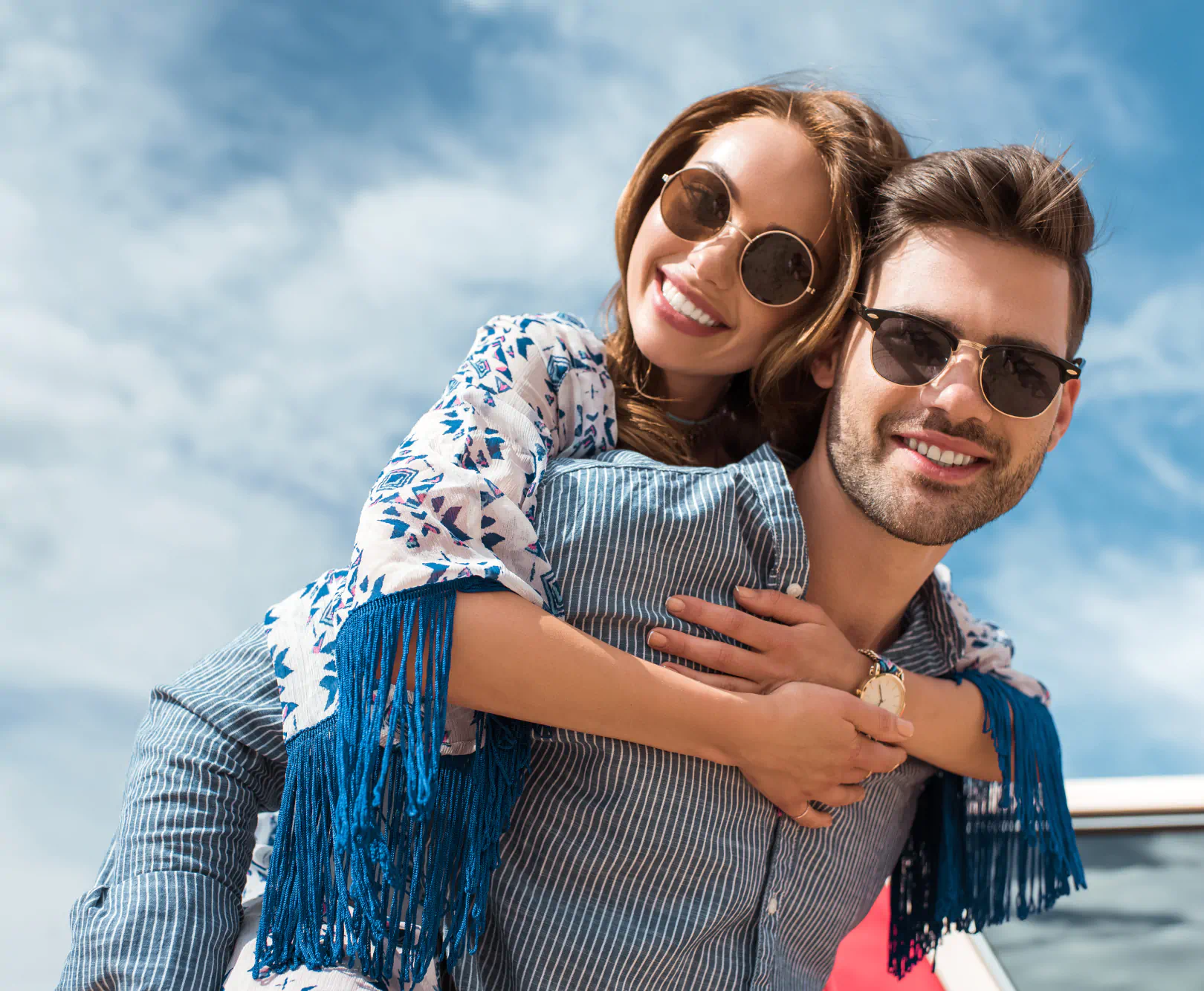 A couple in blue clothes and dark sunglasses embrace outdoors.