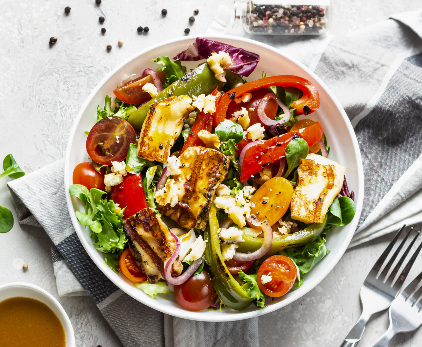 A large bowl of salad topped with chicken sits in a white bowl.