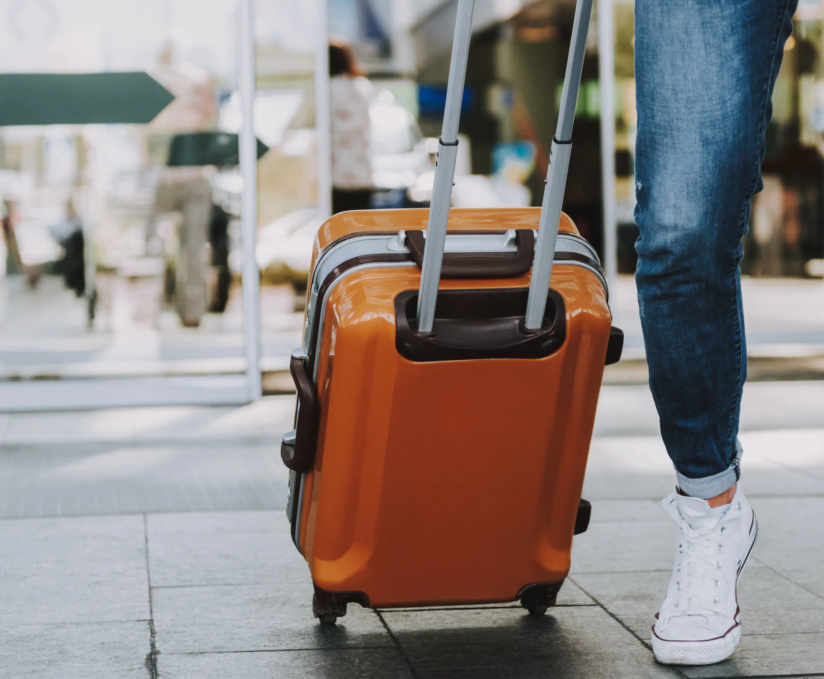 A person walks down the sidewalk with rolling luggage in tow.