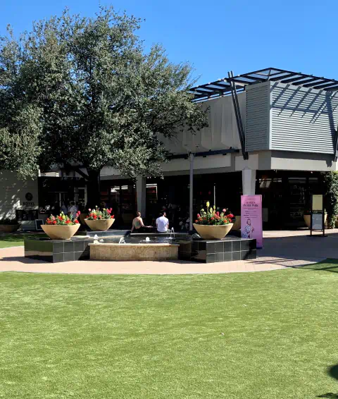 2 people sitting in a plaza with a water feature and grass
