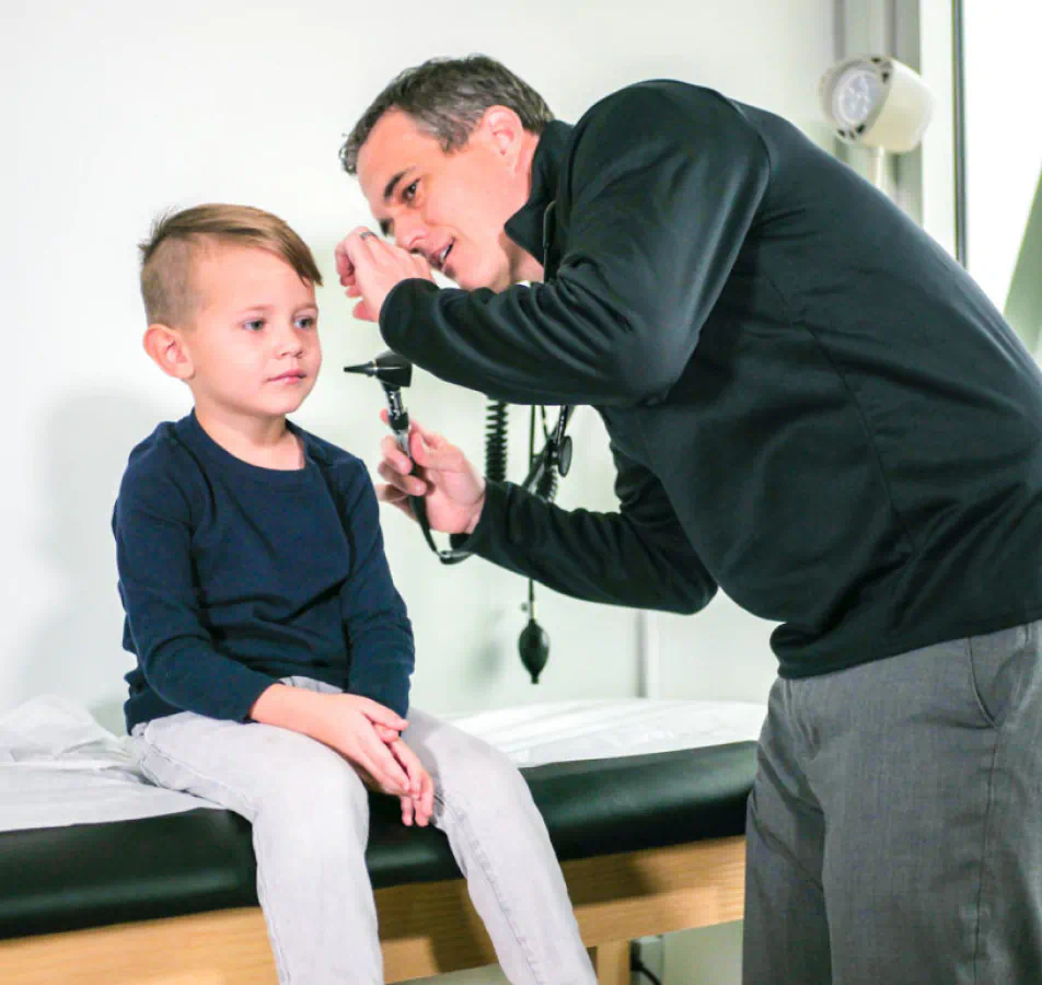 Male doctor using scope to look in childs ear.