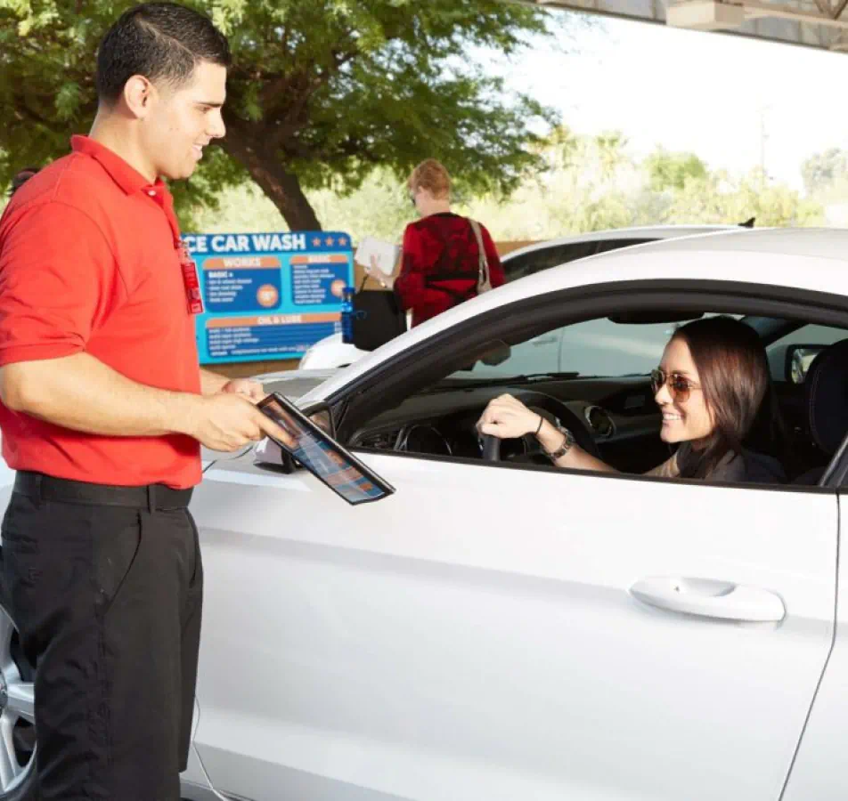 Woman wearing sunglasses driving up to speak to a car wash attendant.