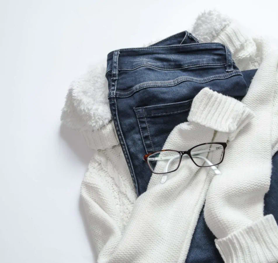 White sweater, jeans and black framed glasses laid out on the floor