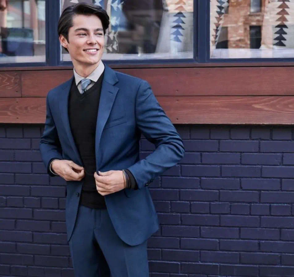 Man posing in nice blue suit and tie standing against a blue painted brick wall with wood panels