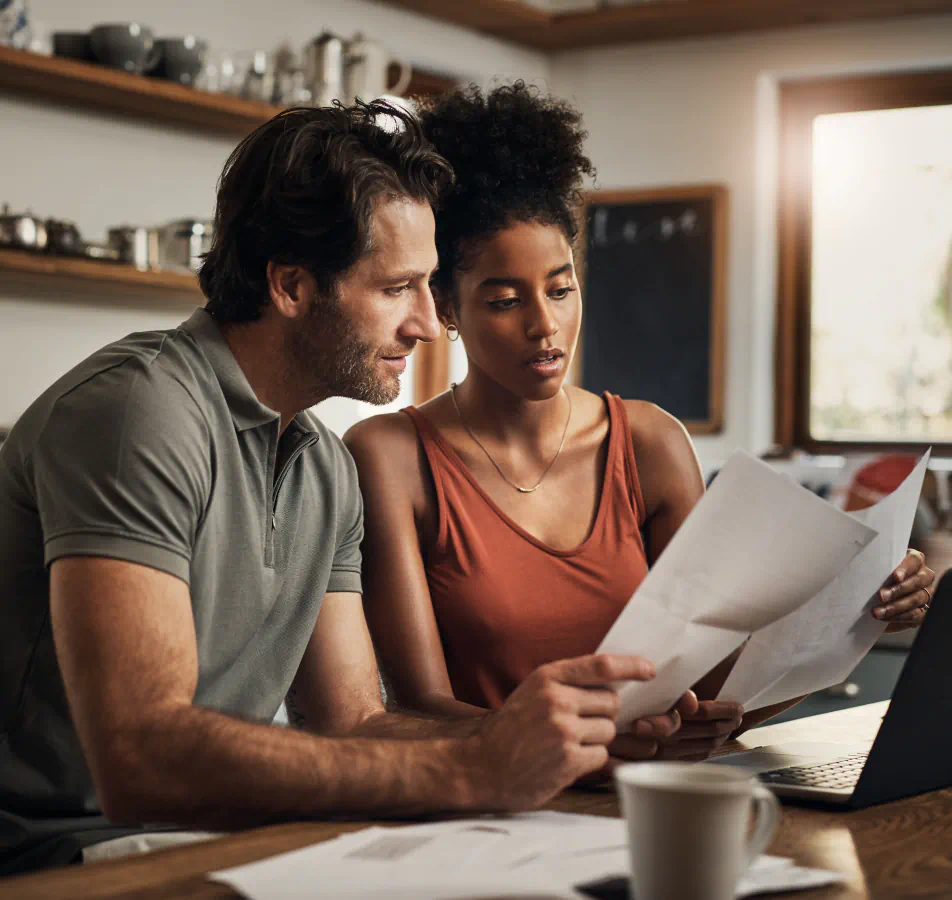 A couple looking at paperwork sitting at a kitchen table with a computer