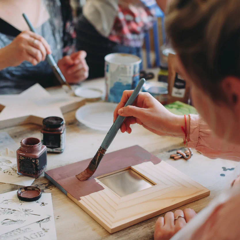 A person paints with purple paint onto wooden frame.
