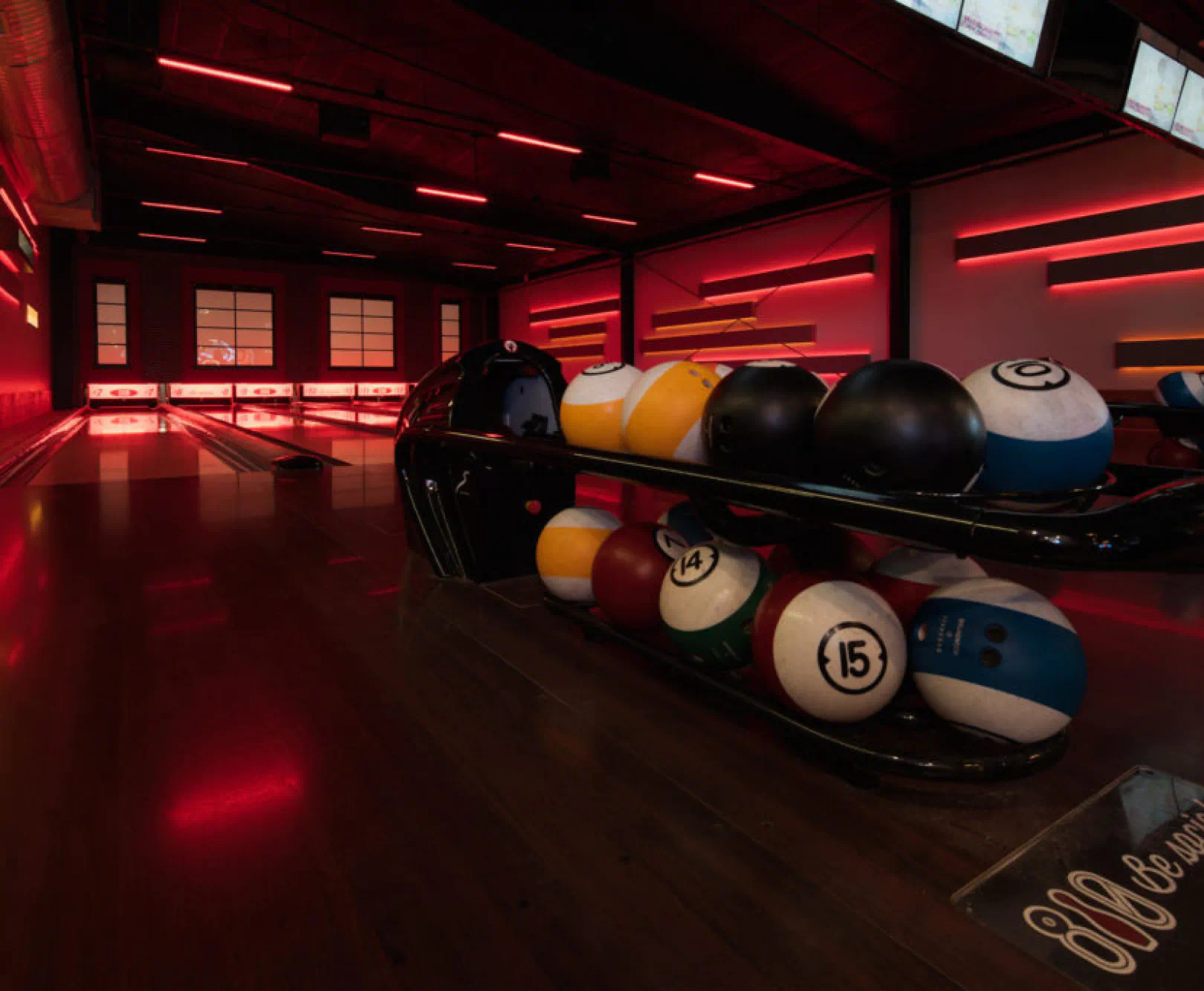 An ambiently lit bowling alley with a bowling ball rack in the foreground