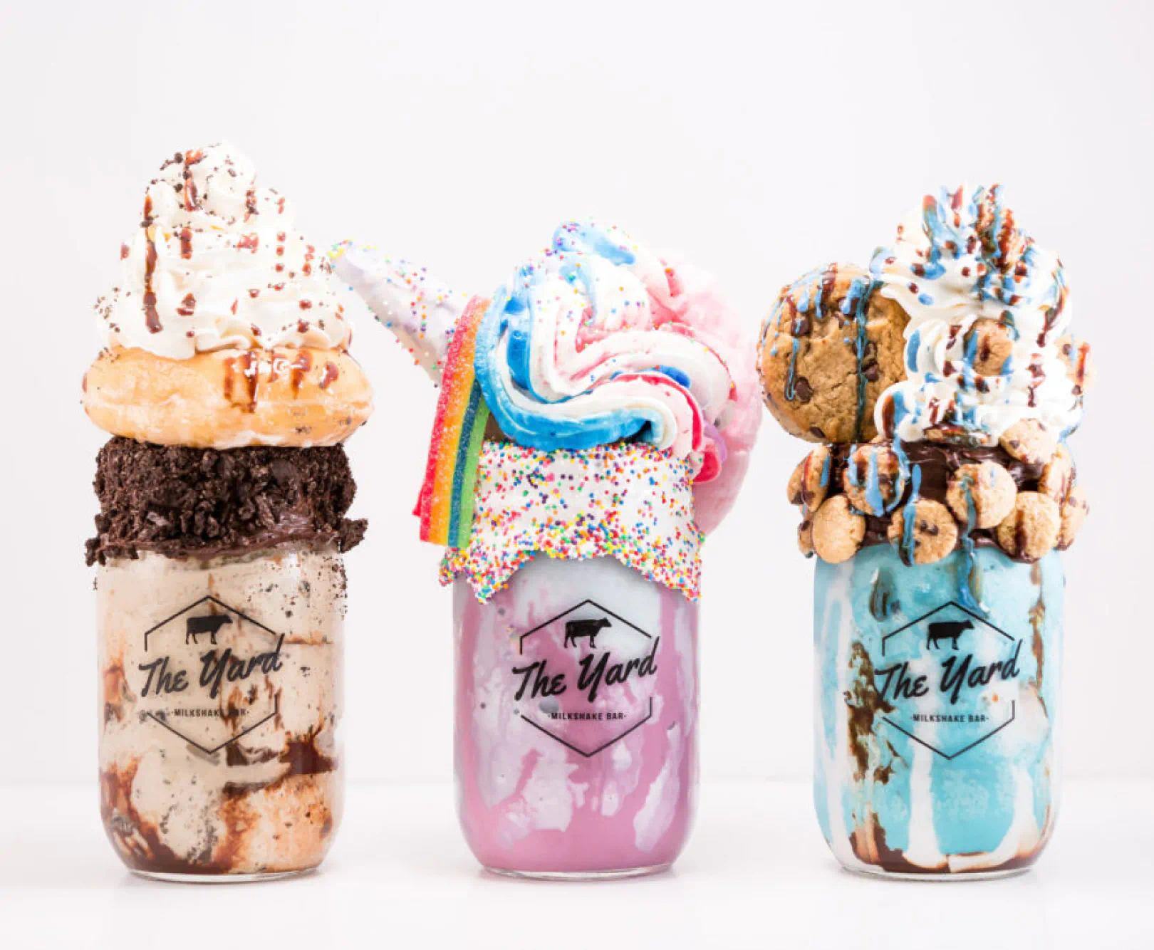 Three colorful and elaborately decorated milkshakes from The Yard Milkshake Bar in glass mason jars.
