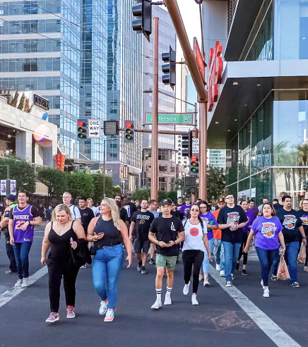 Lots of people in "Phoenix Suns" shirts cross at an intersection in CityScape.