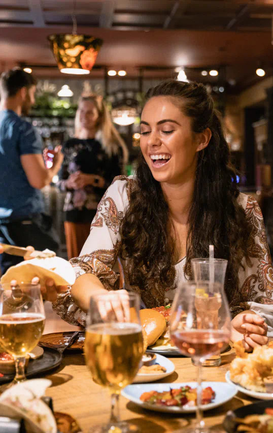 Woman laughing and reaching for food at a restaurant table with drinks.
