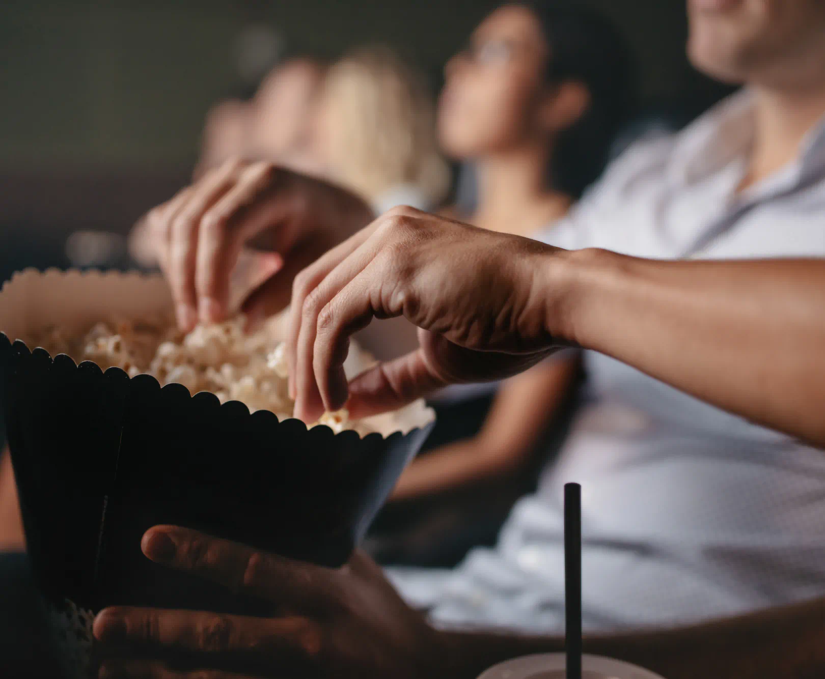 people sitting in a theater reaching into a container of popcorn
