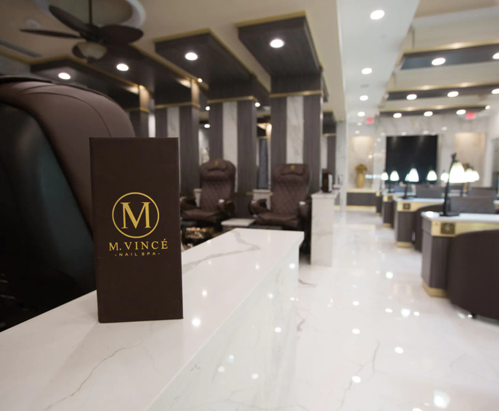 Interior of a nail spa with marble surfaces, dark plush chairs, and a sign that reads "M. Vincé Nail Spa."