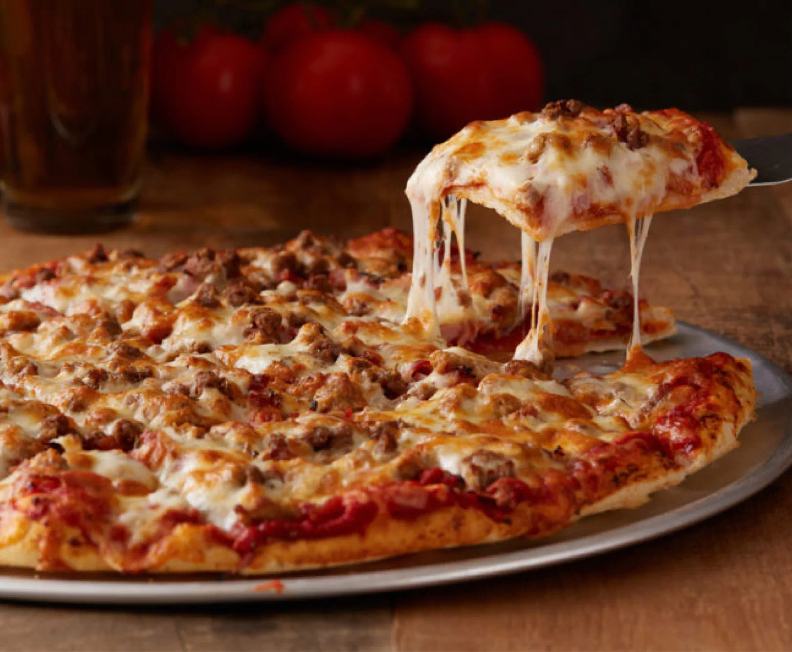 Pizza with melted cheese and sausage, with one slice being lifted, showing the stretchy cheese.