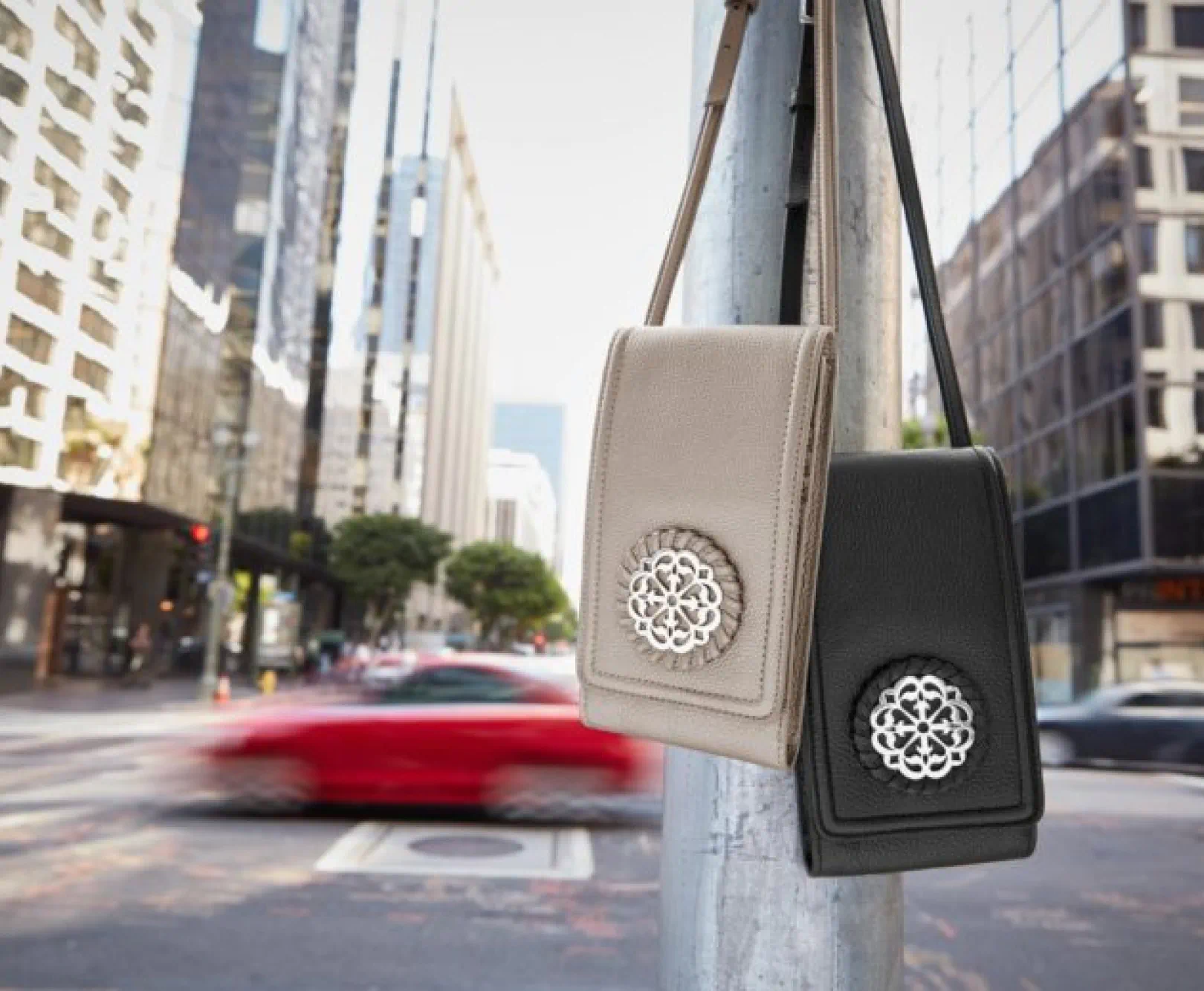 Two handbags hanging from a pole in a busy city street, one beige and one black, with a silver floral medallion on the front.