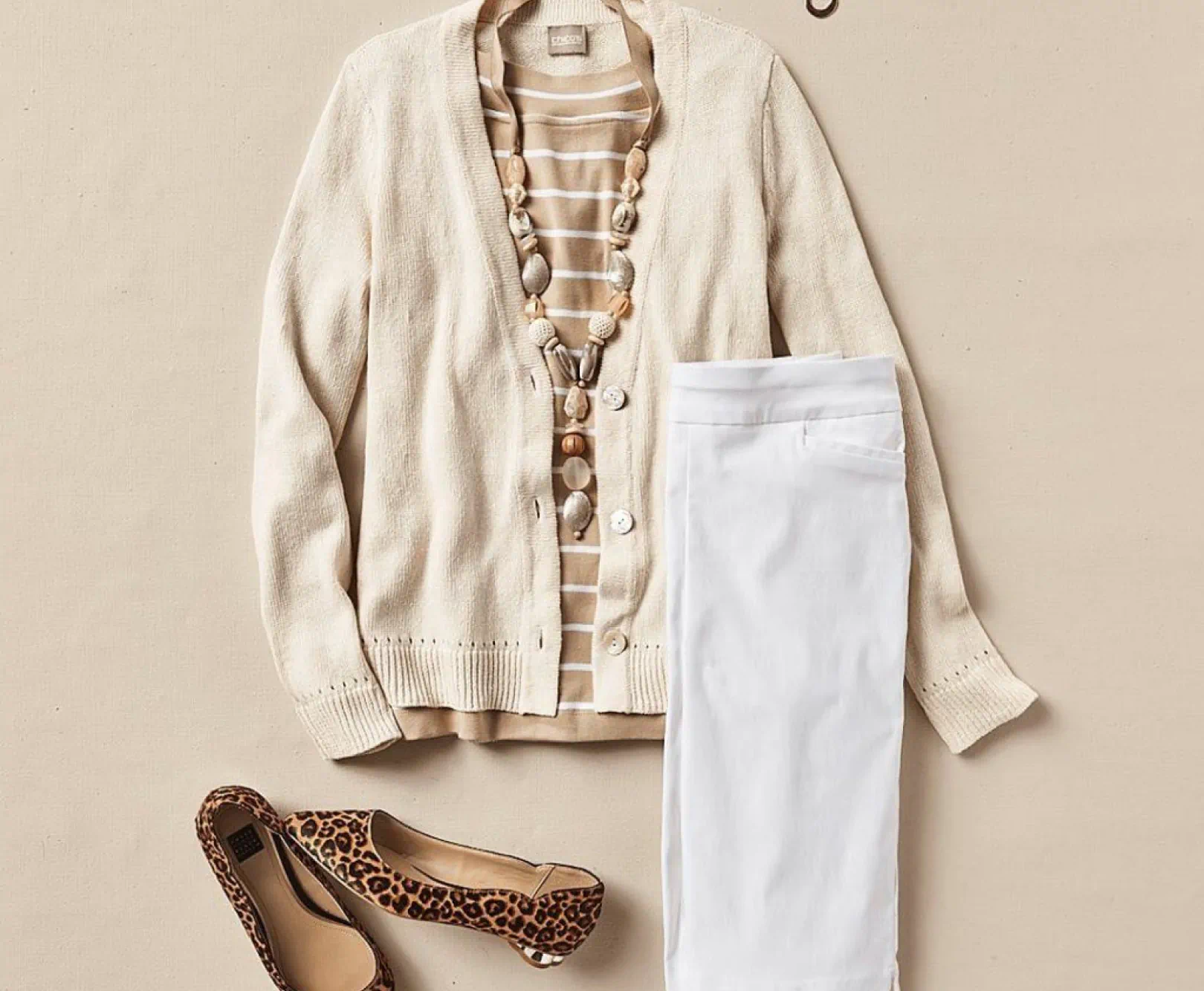 Flat lay of a beige cardigan, striped shirt, white pants, beaded necklace, and leopard-print flats.