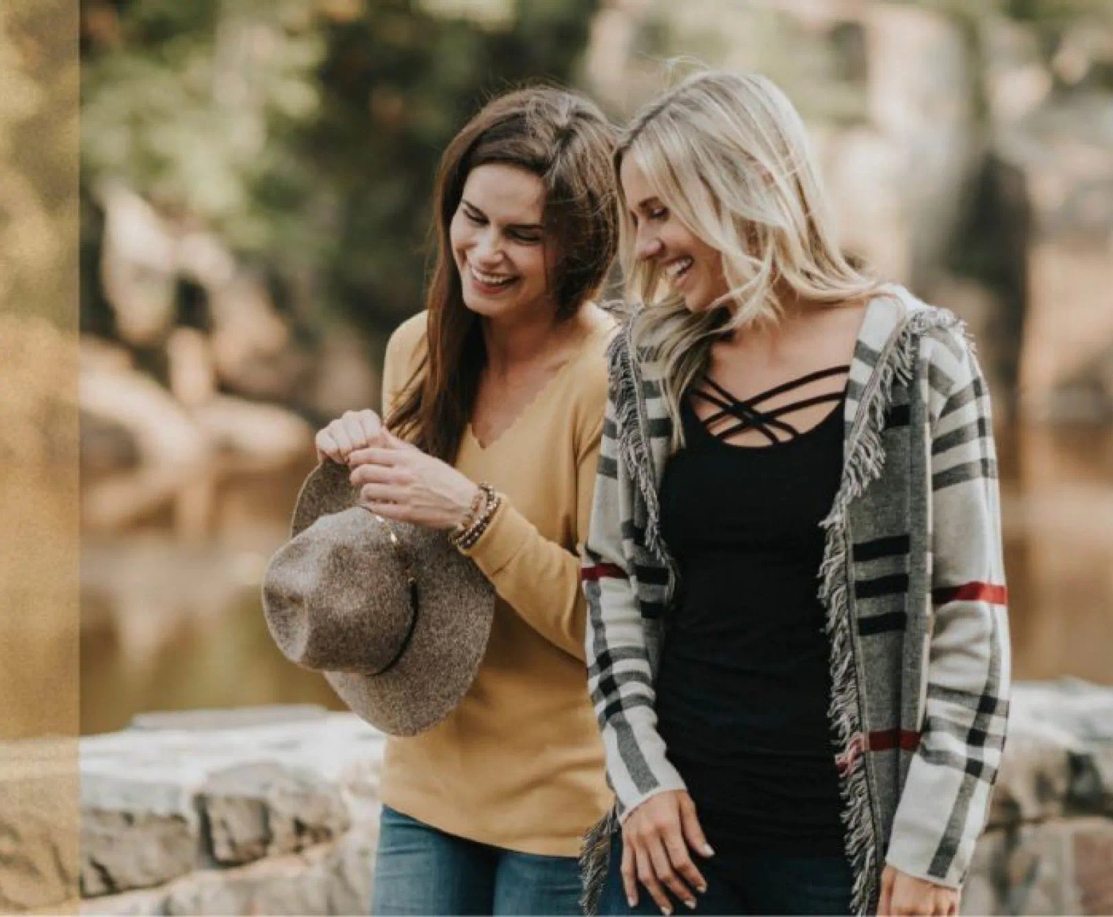 Two women standing together outdoors, smiling, and conversing. One holds a hat.