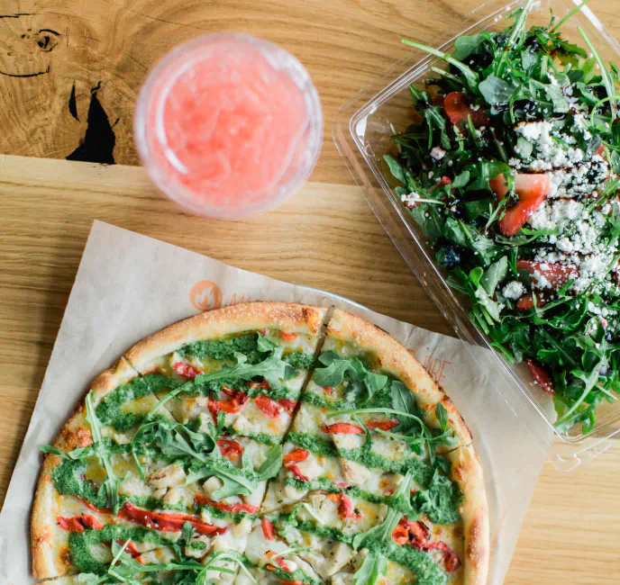 overhead view of a salad, a pizza, and a pink drink on a wooden table.