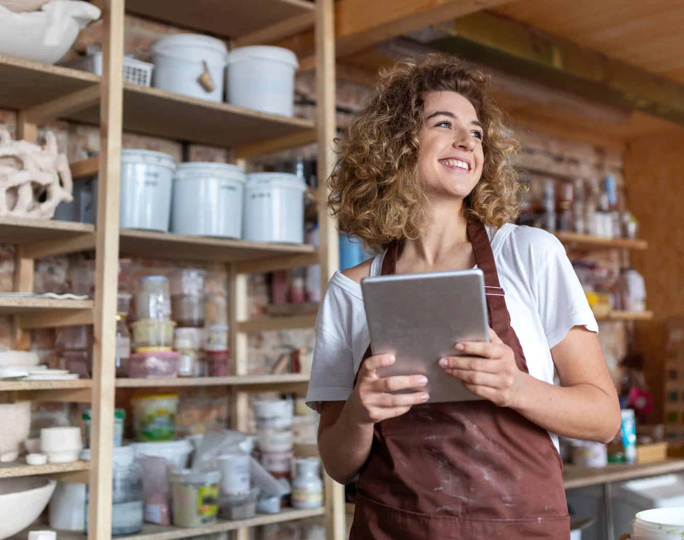 A store owner smiles holding a tablet in a ceramics studio.