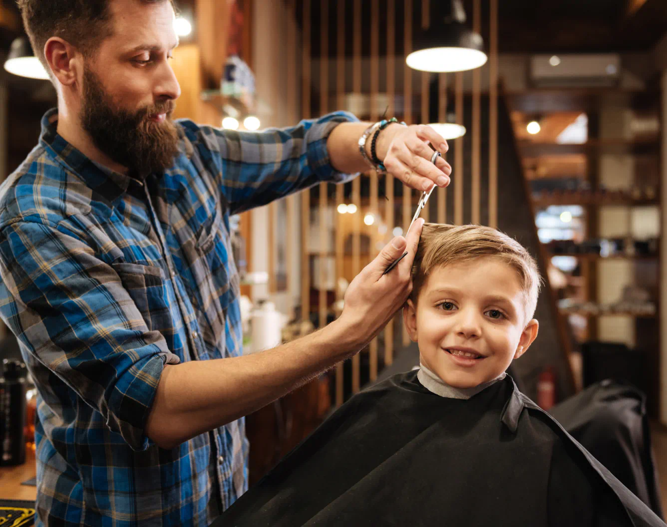 A person trims the blonde hair of a young child in a barber shop.