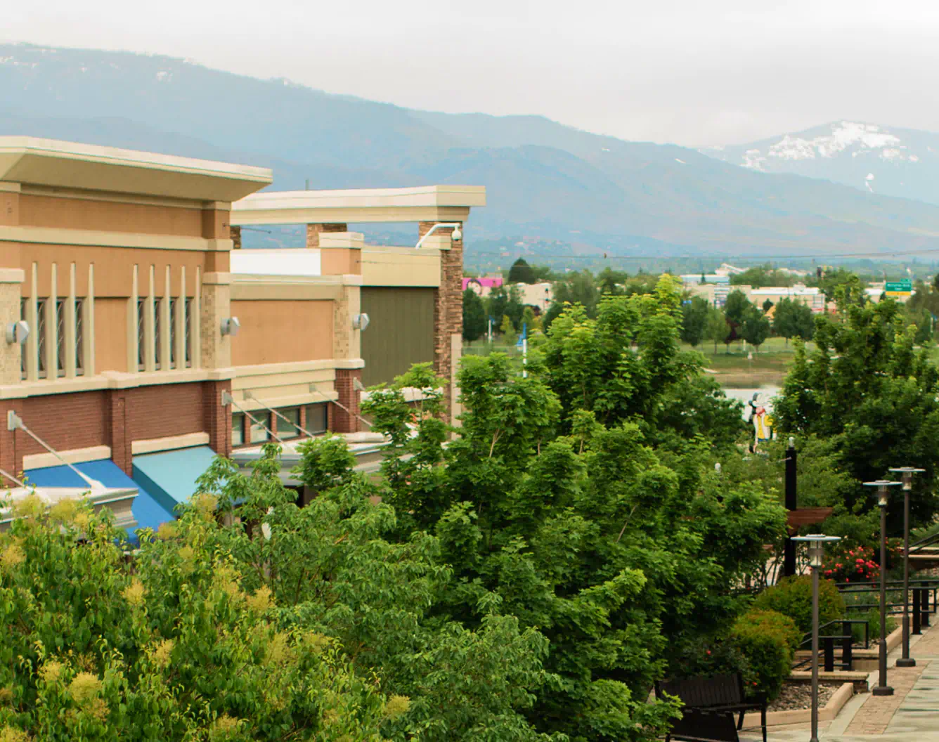 Exterior of the Outlets at Legends, line of trees and stone colored building sit in front of hazy mountains in the background.