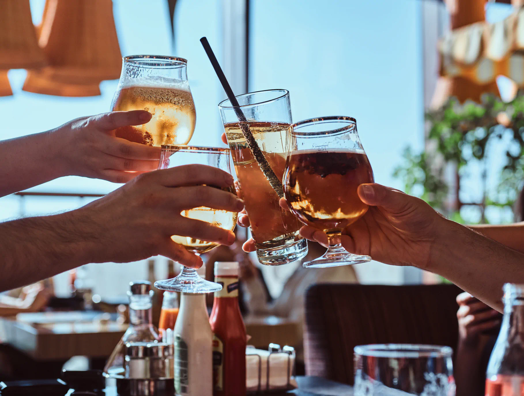Hands clinking glasses of beer and cocktails together at a restaurant.