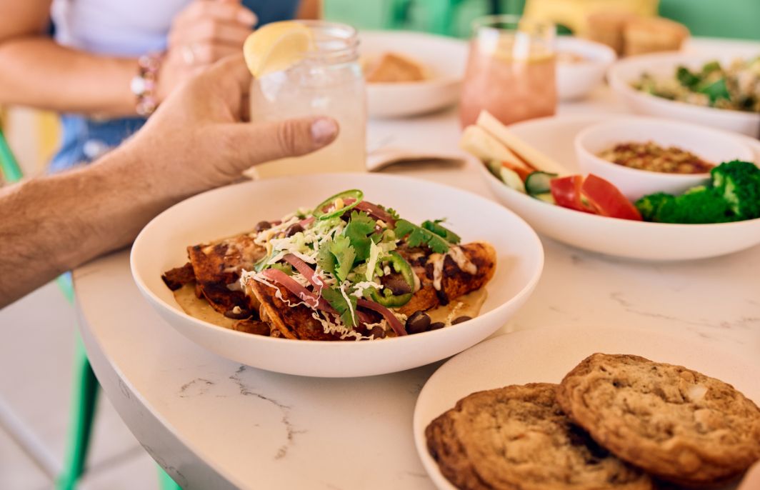 Vibrant food and a plate of cookies sit on a table with glasses of lemonaisw.