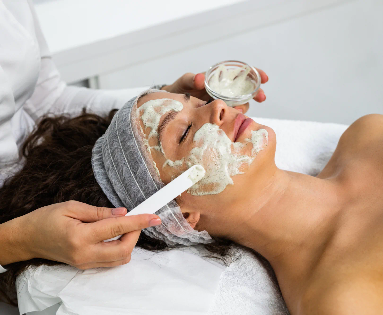 Woman getting a facial with the aesthetician applying a foaming face mask