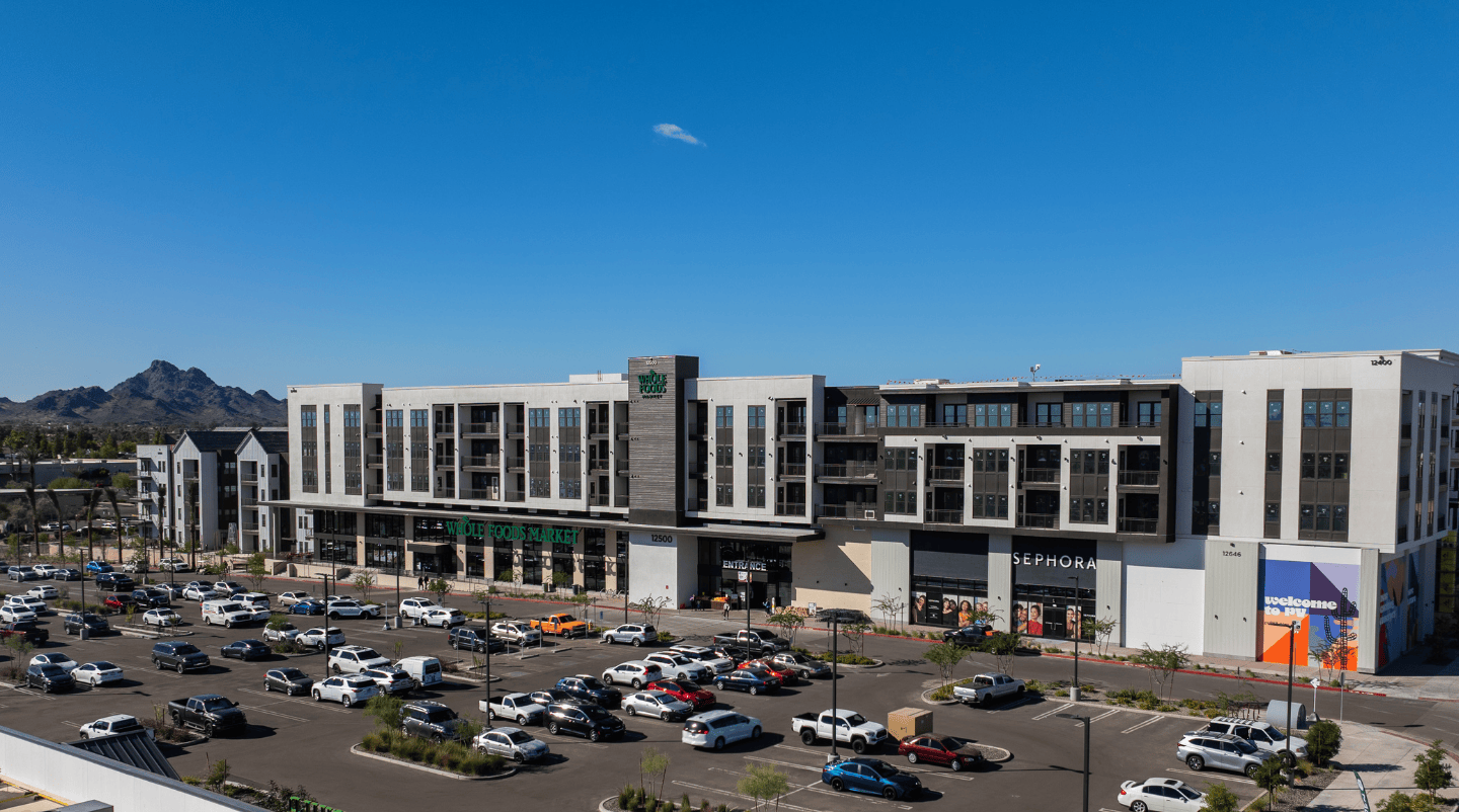 Entrance to shops and the parking lot at Paradise Valley. Many cars parked in front of the storefronts showing "Whole Foods Market", "Sephora", and "Flower Child".