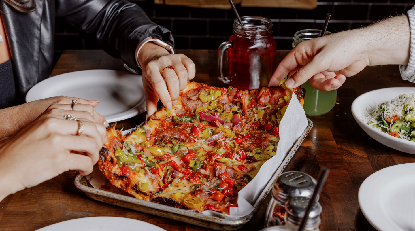 People sharing slices of pizza at a wooden table in a restaurant at Paradise Valley.
