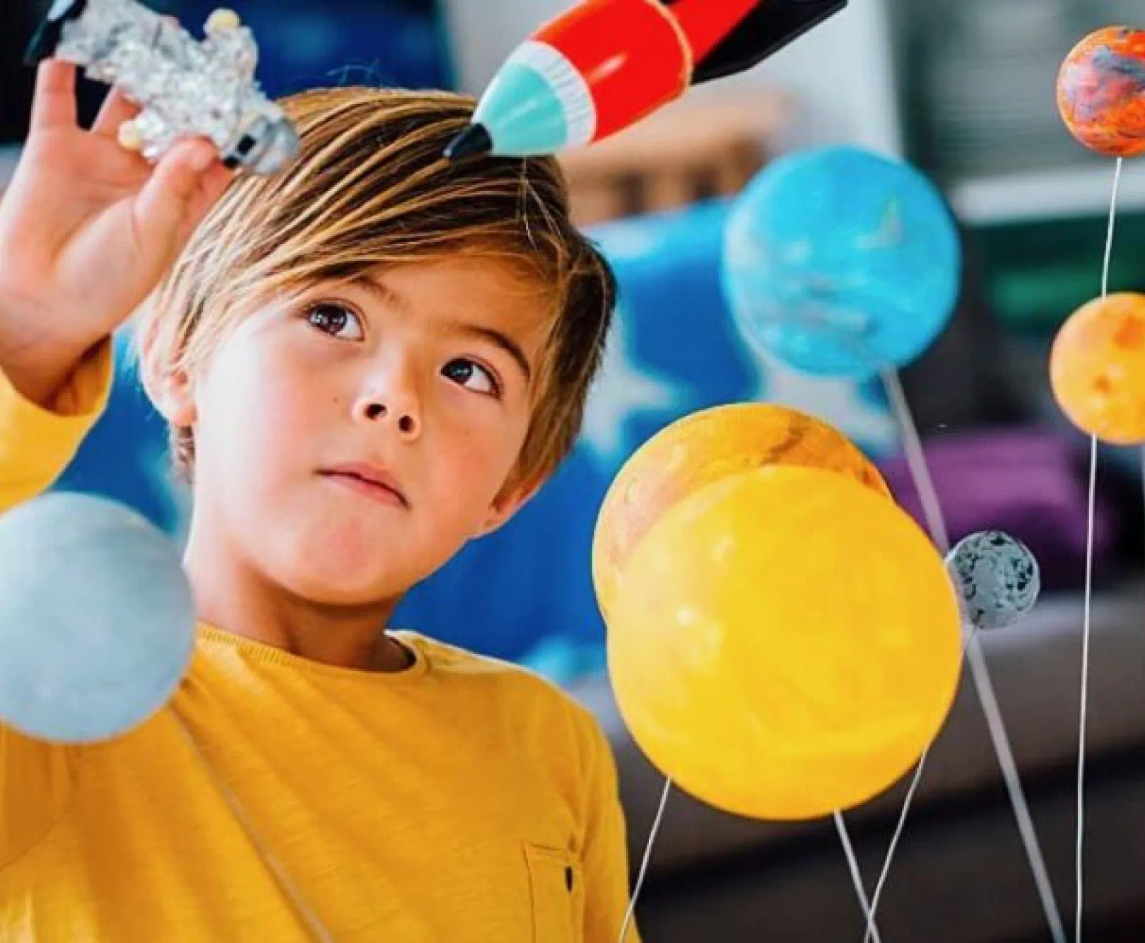 Child holding a model spaceship and looking at a floating solar system model.