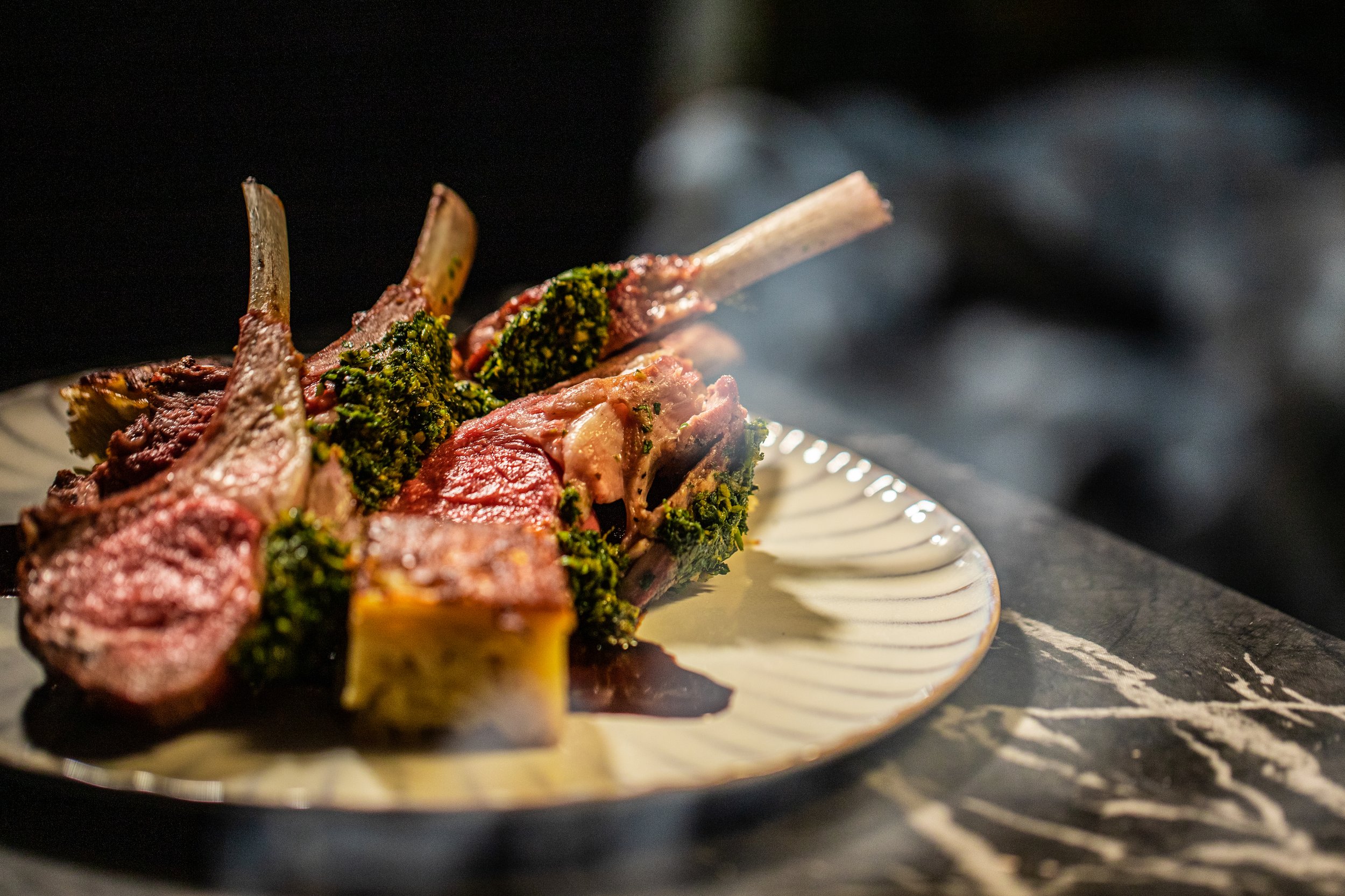 Artfully plated lamb chops with a green sauce on a white plate.