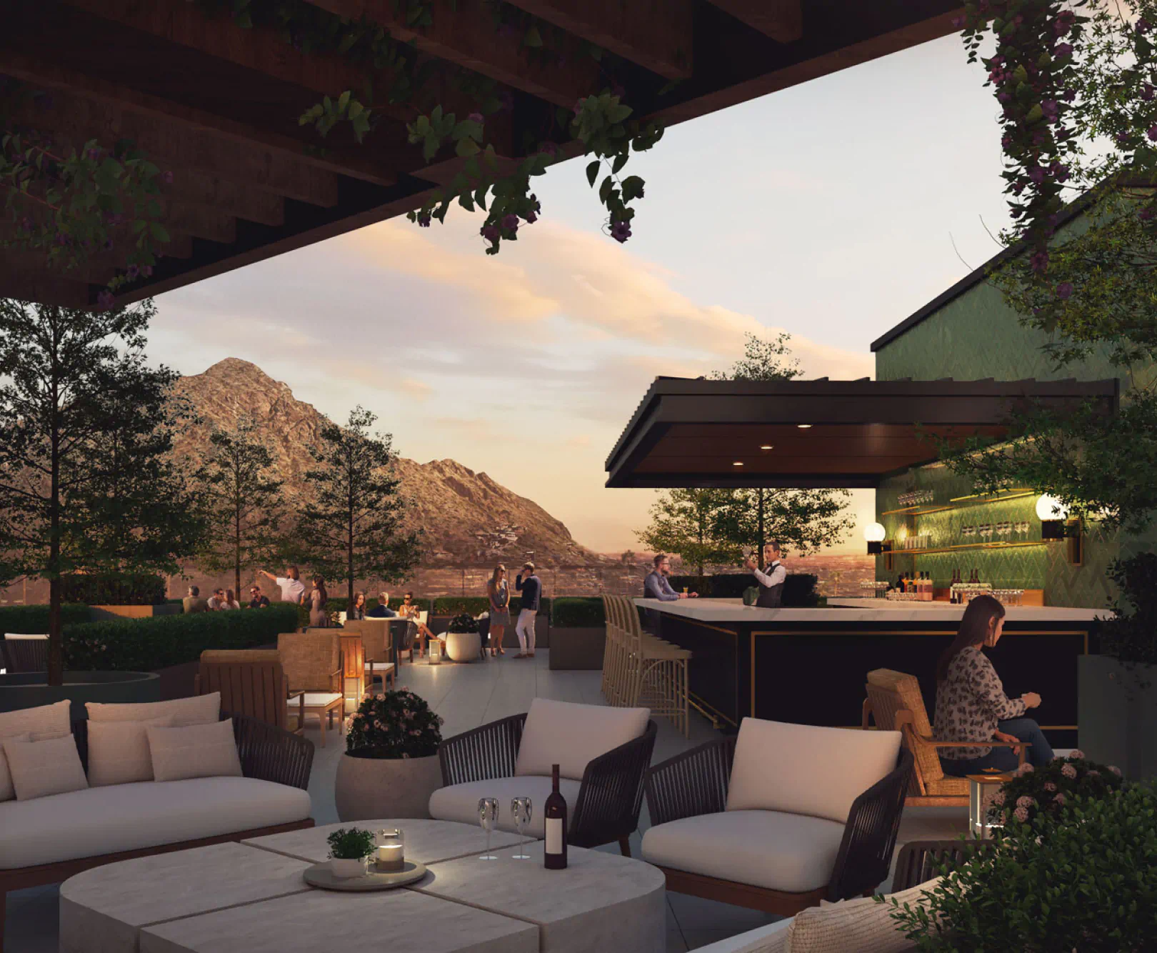 Outdoor terrace bar with modern seating, a bottle of wine and glasses on a stone table, patrons at the bar, and mountains in the background at sunset.