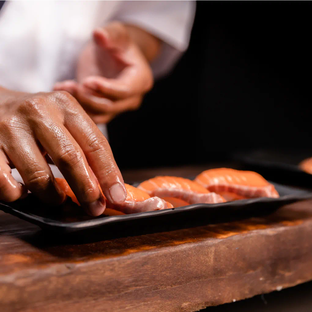 Close-up of hands arranging salmon nigiri on a black platter.
