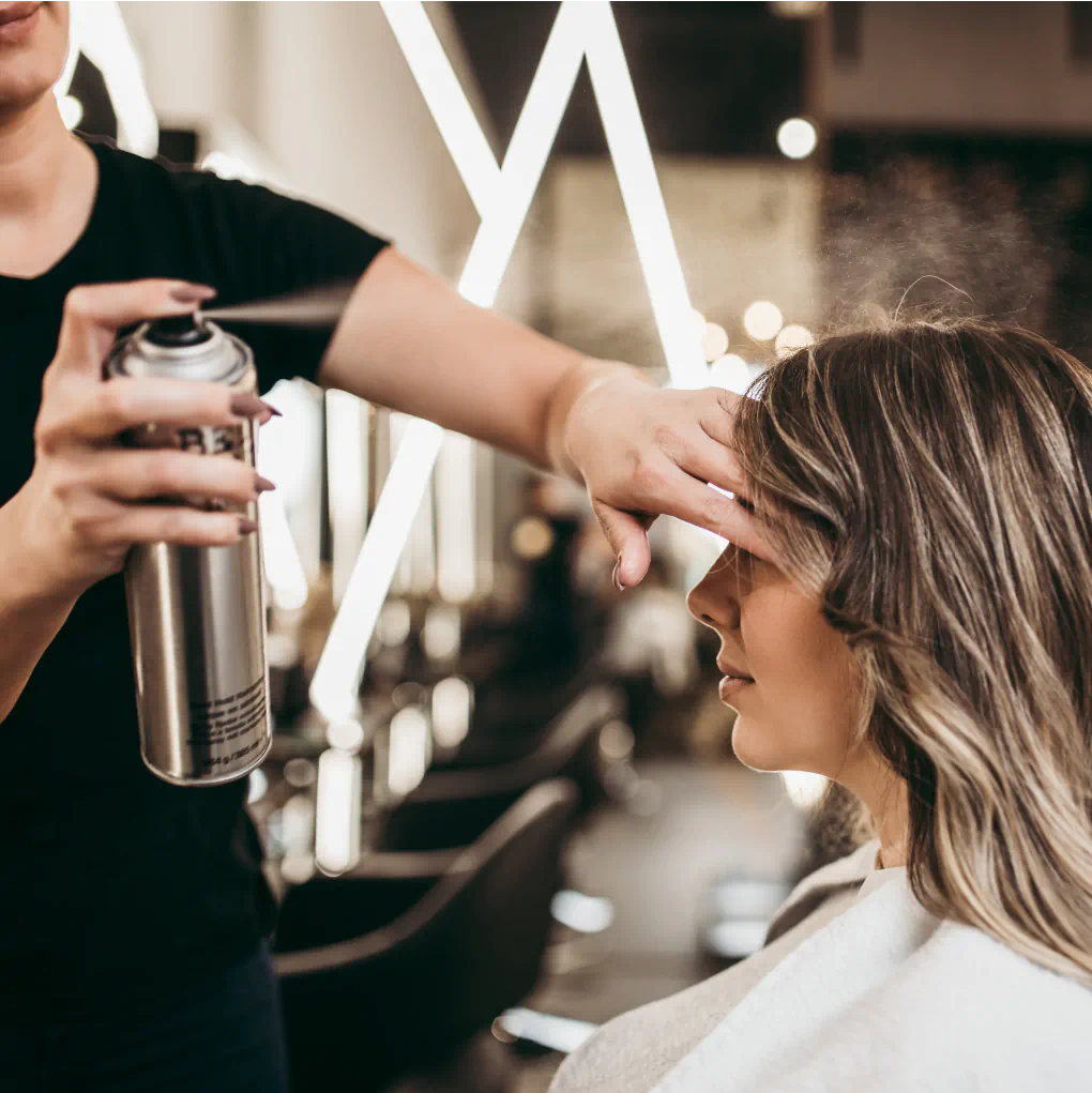 Hair stylist spraying product into a customer's hair in a salon.