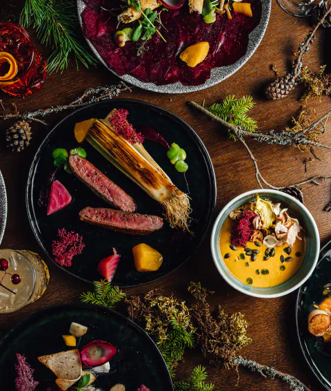 Overhead view of a wooden table with assorted, artfully arranged dishes and natural decorations like pinecones, evergreen sprigs, and moss.