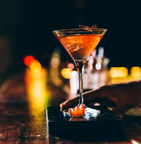 A bright cocktail is served on the bar in a martini glass.