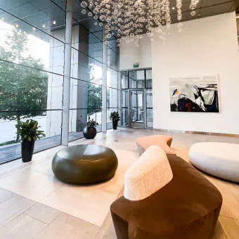 A lobby in The Union features a long brown couch and white ottoman. Tall glass windows make up the wall and a sculpture of glass bubbles is suspended from the ceiling.