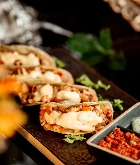 Four artisanal tacos sit on a platter with a small container of salsa.