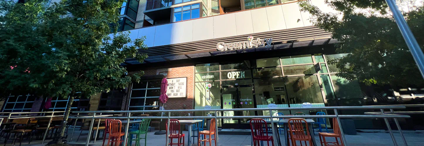 The outside entrance to Creamistry. A sitting area includes metal tables and bright orange chairs.