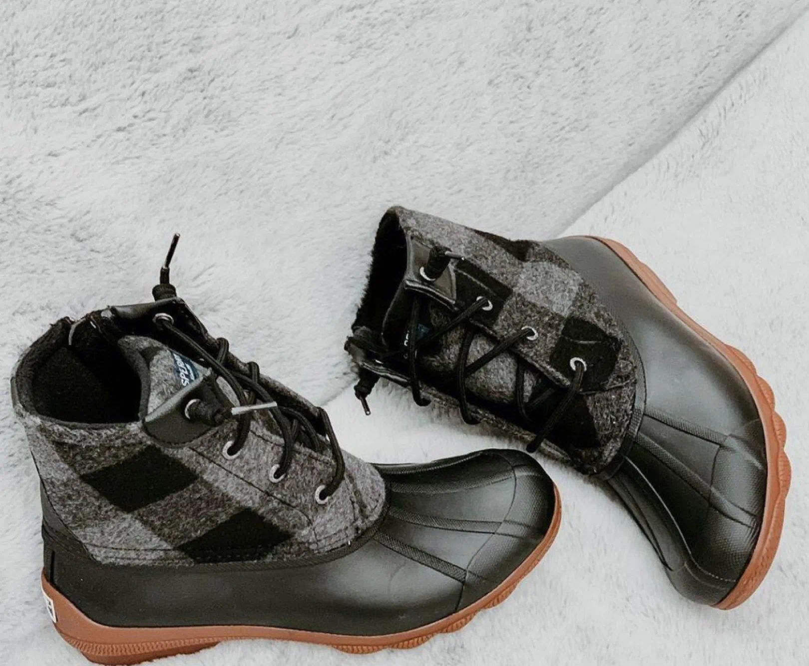 A pair of black snow boots lay on a white fleece blanket.